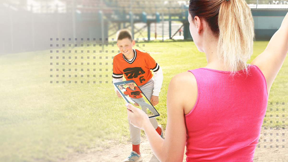 A woman viewing a phone next to a child playing sports