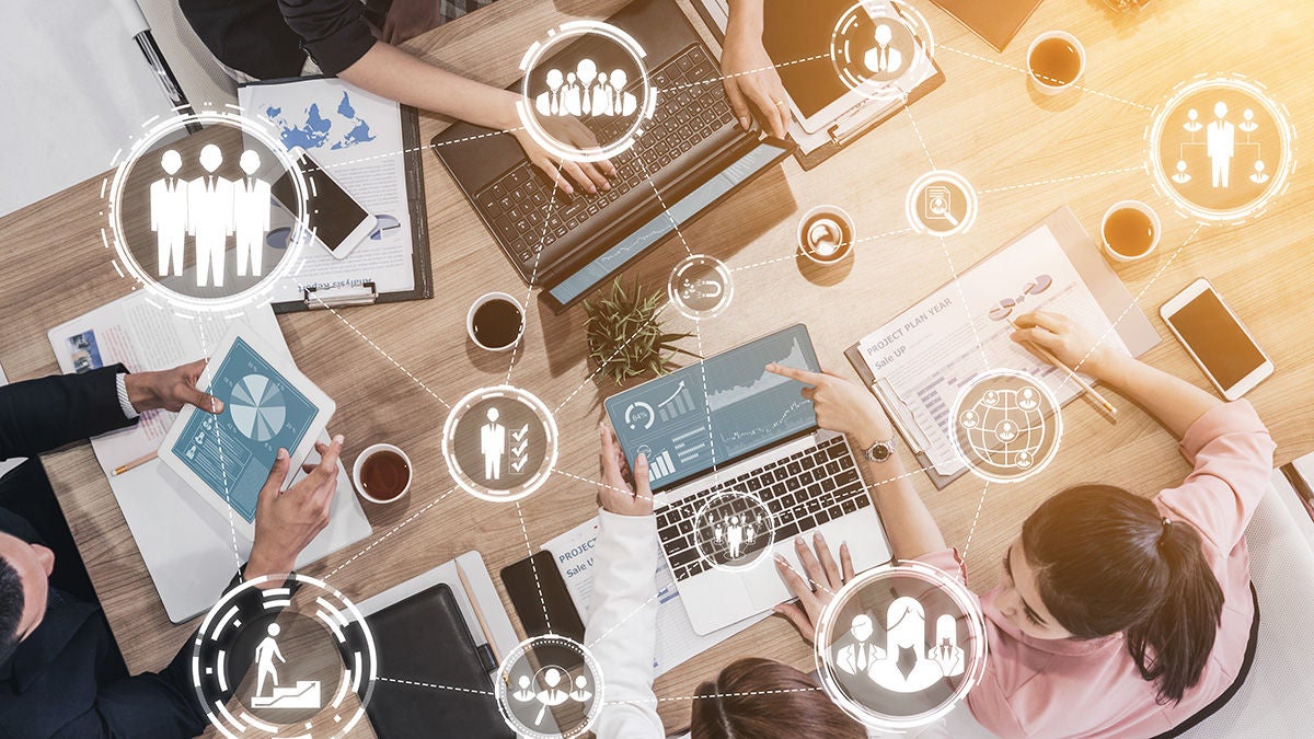 Employees using electronic devices at a table with an overlay of abstract marketing icons