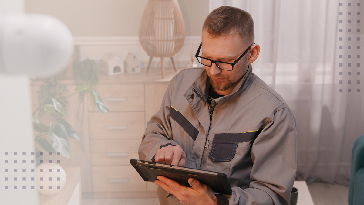 installer in uniform sets up security camera in apartment using digital tablet computer.